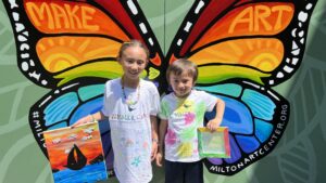 Butterfly mural with two children with summer camp t-shirts holding their art